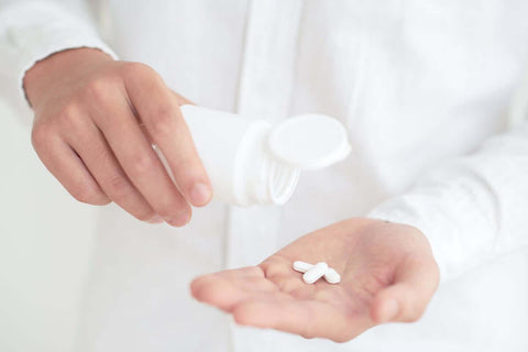 A person pouring supplements into their hand.